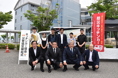 キッチンカーの前にスーツ姿の人たちが並んでいる写真