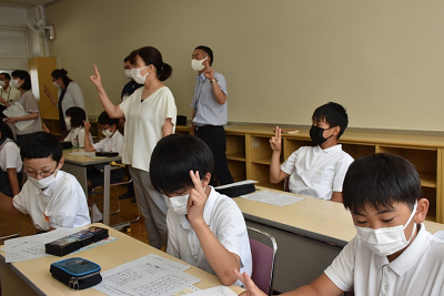 着席して人差し指と中指を立てている児童たちの写真