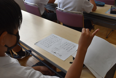 用紙を見ながら右手の小指を立てる児童の写真