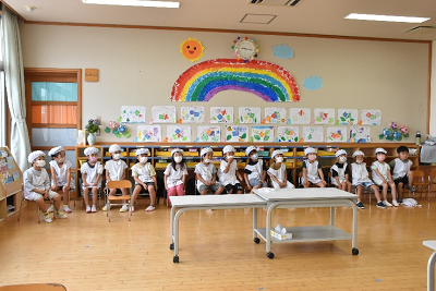 エプロン姿の園児たちがロッカー前に一列に座っている写真