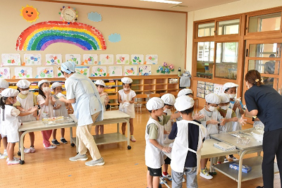 二つのテーブルに別れ、広げた手のひらを大人に見せている園児たちの写真