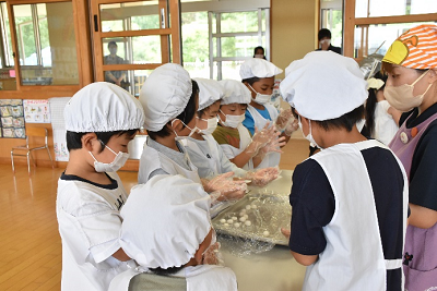 エプロンを着用した女性と園児たちが団子を丸めている写真