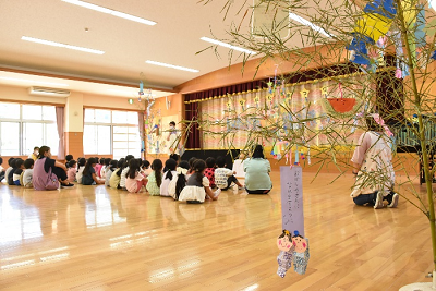 短冊のかかった笹が飾られた室内で園児たちが体育座りしている写真