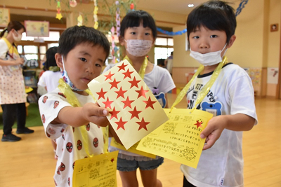 首からかけた黄色の用紙や星形のシールをカメラに向ける園児たちの写真