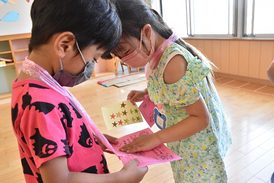 男子園児の持つピンク色の用紙に星形のシールを貼る女子園児の写真