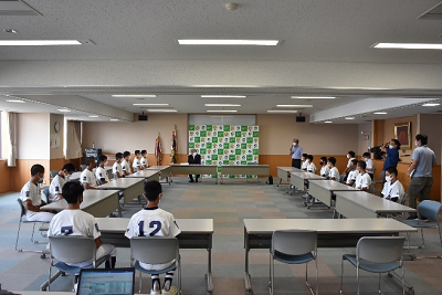 野球のユニフォームを着た人たちが会議室の長机に着席している写真