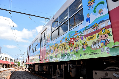 竹笠をかぶった2頭身のゆるキャラが複数描かれた電車を左下のアングルから撮った写真