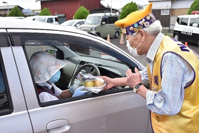 黄色いジャケットを着た人がドライバーに梨を渡して交通安全を呼びかけている写真