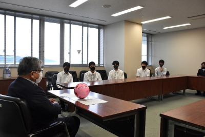 スーツ姿の男性と黒いマスクをした人たちが向き合っている写真