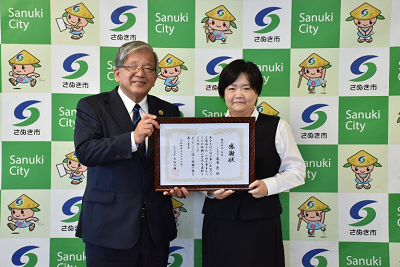 スーツを着た男女が感謝状を2人で持っている写真