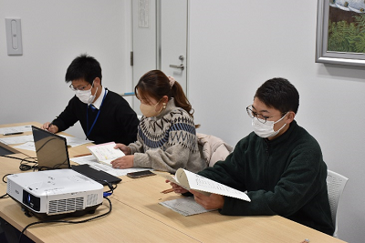 3人の男女が座って手元の資料を見ている写真