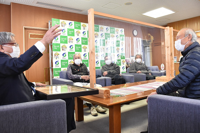 アクリル板の置かれたテーブルの周りで座りながら話をしている人たちの写真