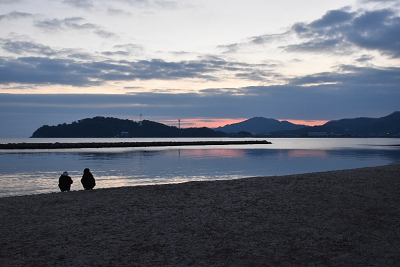 朝焼けしている砂浜で座っている人たちの写真