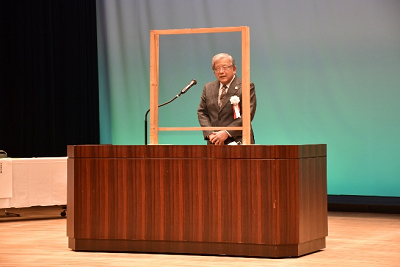 演台で話すスーツ姿の男性の写真