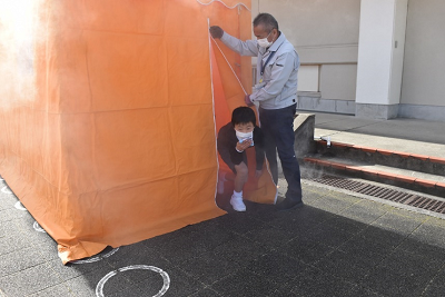 煙の出ているテントから身をかがめて出てくる児童の写真