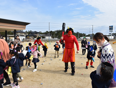 赤鬼の仮装をした大人から逃げたり豆を投げたりしている園児たちの写真