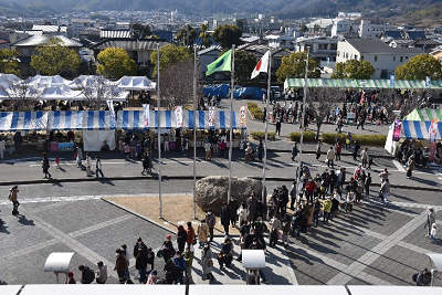 日本国旗が飾られ、テントが設置された広場に人々が並んでいる写真