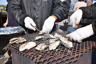 網で焼かれた牡蠣をナイフで剥いている写真