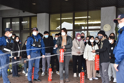 消防団員が見守る中、消火器を噴射する男女の写真