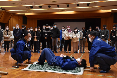 体育館で人を乗せた担架を持ち上げようとしている2人の男性の写真