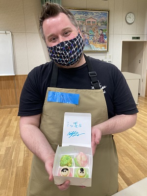 完成した生菓子4種が入った箱を持ち、カメラに向けて見せる男性の写真