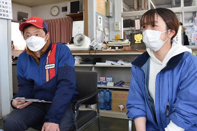 青色のジャケットを着用した男女2人が並んで座っている写真