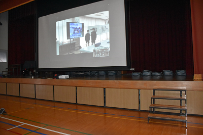 壇上で展開されているスクリーンに映像が写っている写真