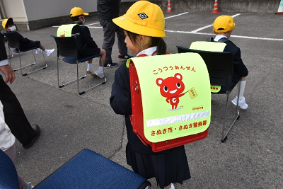 こうつうあんぜんと書かれたランドセルカバーをカメラに向けている児童の写真