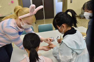 ウサギ耳のカチューシャをつけた金髪の女性が児童たちにカラフルなチョコレートを渡している写真