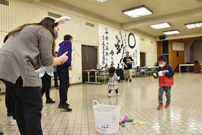 卵型のボールを白いかごへ運ぶ男子児童と見守るウサギ耳のカチューシャをつけた女性の写真