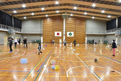 体育館の床に置かれたかごや遊んでいる児童たちの写真