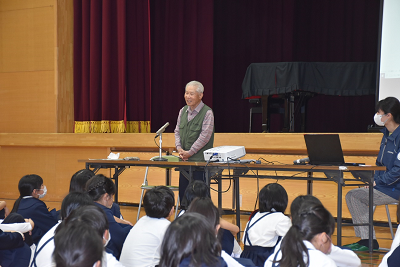 体育座りした生徒の前で立って話す男性の写真