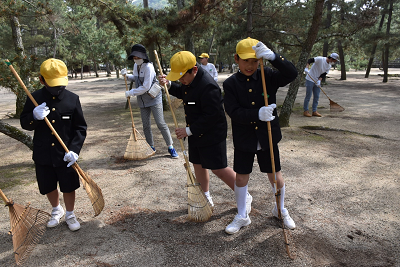 3人の男子児童が熊手を使い掃除を行っている写真