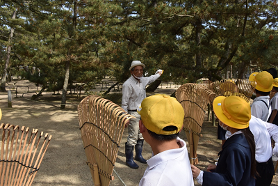 説明を行う男性と向かい合って、熊手をもって一列に並ぶ児童たちの写真