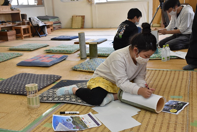 竹の上に置いた紙に書き込む少女の写真