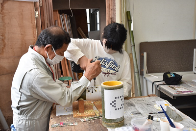 作業服の男性と少女が電動ドリルで竹に穴をあけている写真