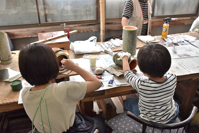 椅子に座り、竹の中に色を塗っている2人の子供の写真