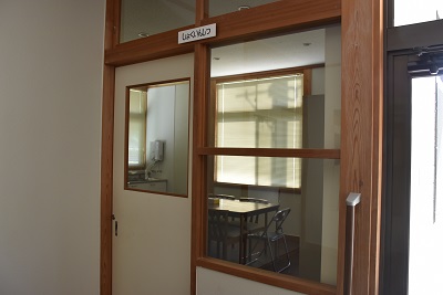 扉や壁に備え付けられたガラスから部屋の中の机やパイプ椅子が見える写真