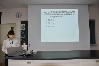 スクリーン横でノートパソコンを操作する女性の写真