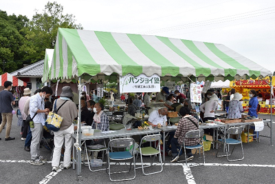 緑と白の縞模様のテント下にテーブルとパイプ椅子が設置されている写真