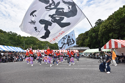 大きな旗を振る男性と踊る和装姿の人々の写真