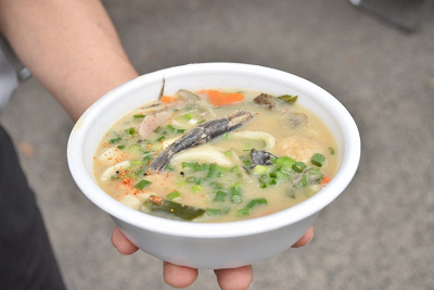 使い捨てカップにねぎやニンジンが入ったうどんが盛られている写真