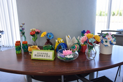 折り紙で作られたフクロウや色とりどりの花が飾られた机の写真