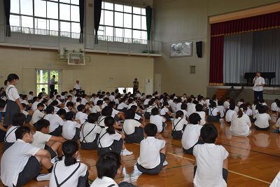 座る児童の中で一人立つ女子児童の写真