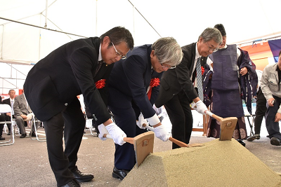 男性3人が小さい土の山に鍬入れをしている写真