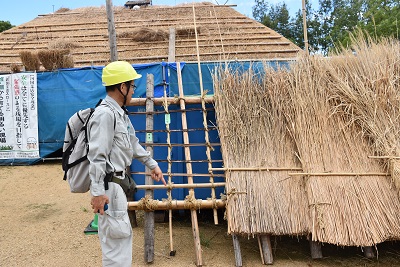 作業中の建物の前で作業服にヘルメットを着用した男性が立っている写真