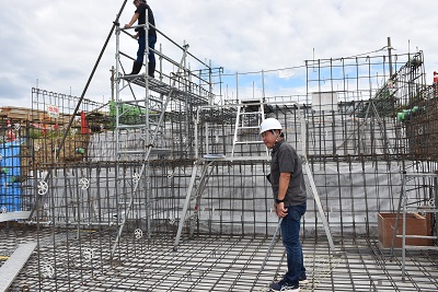 はしごが組まれた建物の基礎に乗って周りを見ている写真
