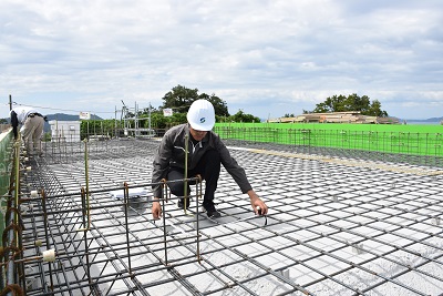 ヘルメットを着用した人がメジャーで鉄筋を確認している写真
