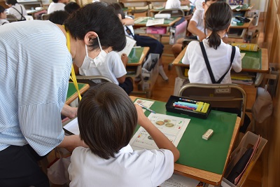 着席した生徒の横で中腰になり、児童と話す女性の写真