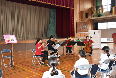 児童の前で弦楽器を演奏する4人の写真